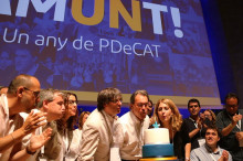 Pla contrapicat de Carles Puigdemont, Artur Mas i Marta Pascal bufant l'espelma del primer aniversari del PDeCAT, amb l'eslògan 'Un any de partit' al darrere. Imatge del 8 de juliol de 2017