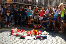 Un grup de gent mirant les flors i les espelmes dipositades en homenatge a les víctimes de l'atemptat el 18 d'agost de 2017
