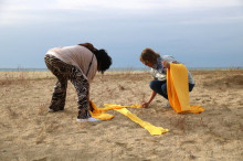Dues dones estenen teles de tovallola groga en forma de creu a la platja de Mataró