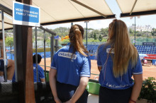 Pla mig de dues voluntàries a la graderia de les pistes de tenis, d'esquenes, als Jocs Mediterranis