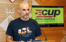 Pla mig del regidor de la CUP de Tortosa, Xavier Rodríguez, davant d'una pantalla amb les sigles del partit, a la sala de premsa de l'Ajuntament