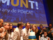 Pla contrapicat de Carles Puigdemont, Artur Mas i Marta Pascal bufant l'espelma del primer aniversari del PDeCAT, amb l'eslògan 'Un any de partit' al darrere. Imatge del 8 de juliol de 2017