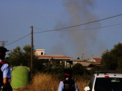 Pla mig de la columna de fum amb dos agents dels Mossos d'Esquadra d'esquena durant la detonació controlada
