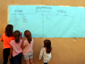 Pla americà d'un grup de nenes davant un cartell del concurs de pedra, paper i tisora de l'escola Enric Casassas