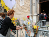 Una dona lliga una rosa groga a la tanca que protegeix l'entrada del Palau de la Generalitat, la diada de Sant Jordi 2018