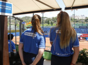 Pla mig de dues voluntàries a la graderia de les pistes de tenis, d'esquenes, als Jocs Mediterranis